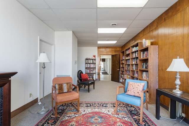 sitting room with carpet flooring, a paneled ceiling, wooden walls, and built in shelves