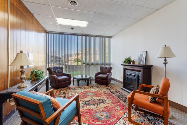 carpeted living area with baseboards, visible vents, a drop ceiling, and a glass covered fireplace