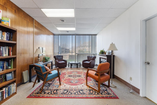 living area with a drop ceiling, wooden walls, and light carpet