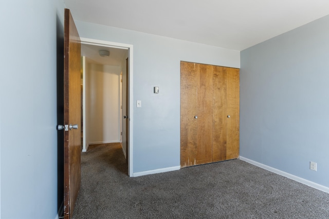 unfurnished bedroom featuring baseboards, a closet, and dark colored carpet