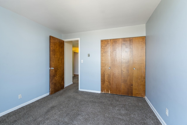 unfurnished bedroom with dark colored carpet, baseboards, and a closet