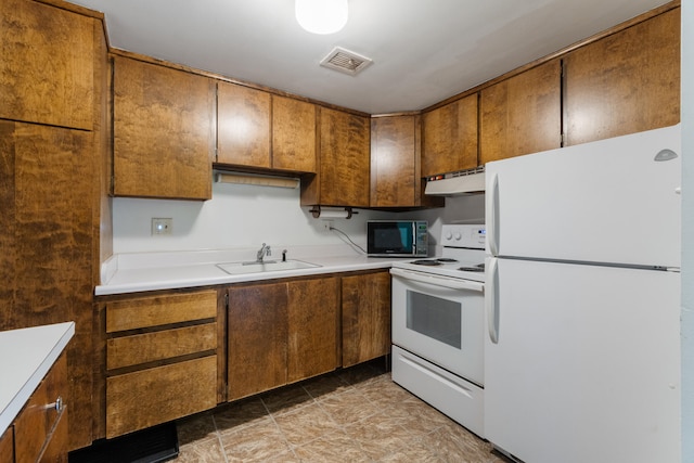 kitchen featuring white appliances, light countertops, under cabinet range hood, brown cabinets, and a sink