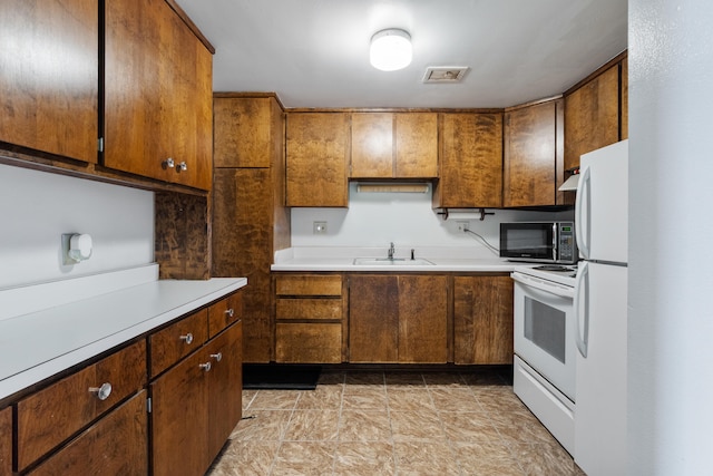 kitchen featuring visible vents, brown cabinetry, white appliances, light countertops, and a sink