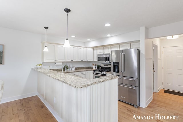 kitchen with light wood-style flooring, a peninsula, light stone countertops, and stainless steel appliances
