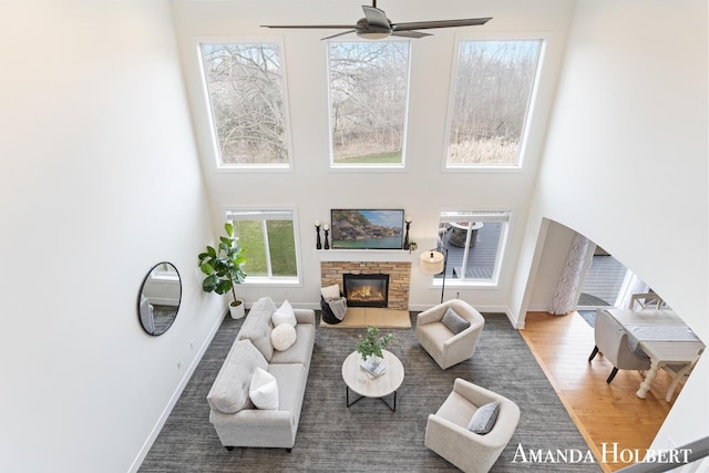living area with a high ceiling, a stone fireplace, wood finished floors, and ceiling fan