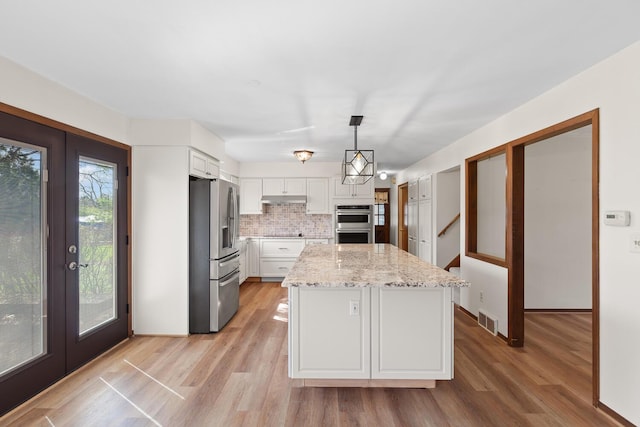 4675 Treat Hwy, Adrian, MI 49221 - kitchen with white cabinets, under cabinet range hood, visible vents, appliances with stainless steel finishes, and light wood finished floors