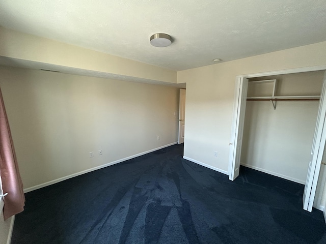unfurnished bedroom featuring a closet, baseboards, and dark carpet