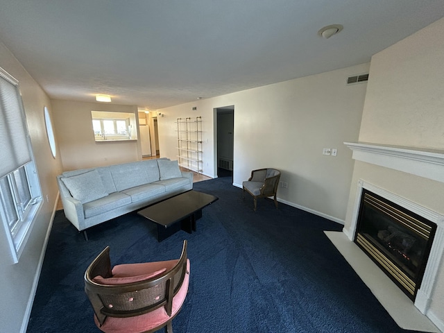 living room featuring dark carpet, baseboards, visible vents, and a fireplace with flush hearth