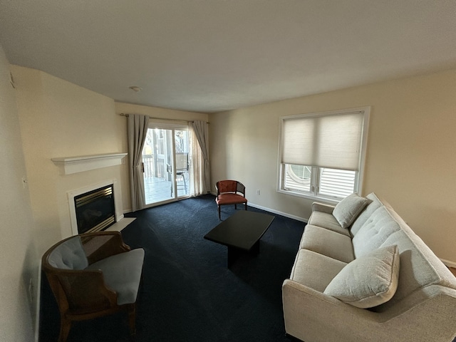living area with a glass covered fireplace, dark colored carpet, and baseboards