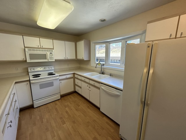 kitchen with light wood-type flooring, white appliances, light countertops, and a sink