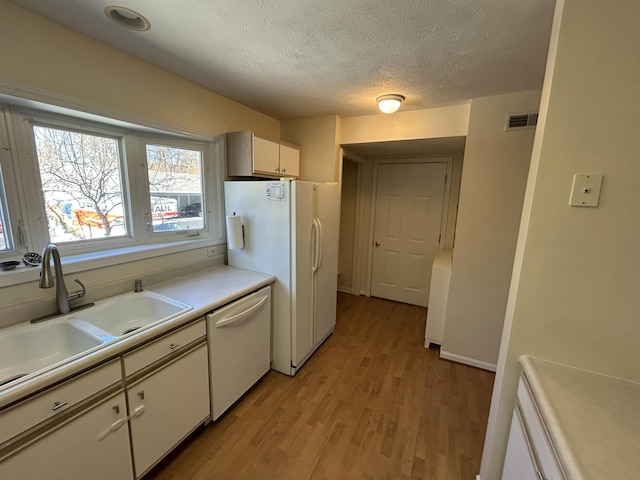 kitchen with visible vents, a sink, light countertops, white appliances, and light wood finished floors