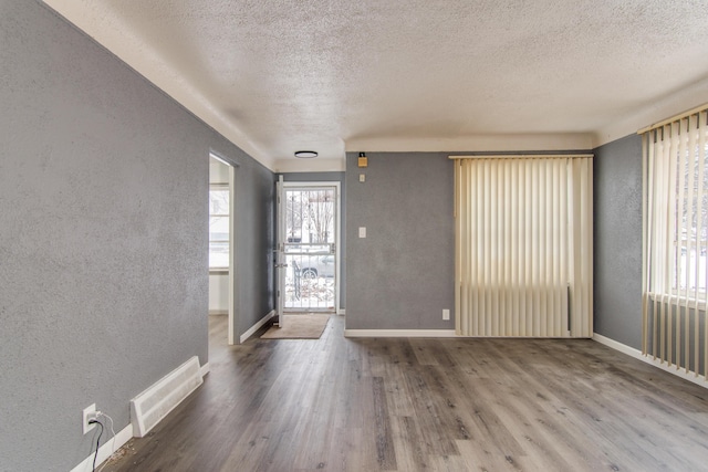 entrance foyer with visible vents, baseboards, wood finished floors, and a textured wall