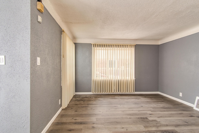 empty room featuring a textured wall, a textured ceiling, and wood finished floors