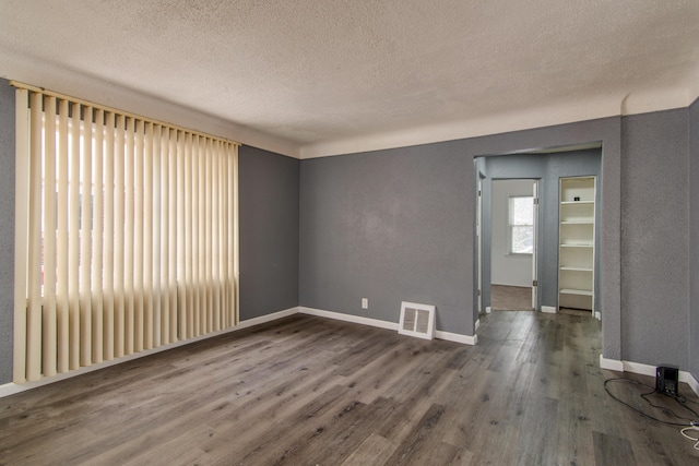 empty room featuring visible vents, a textured ceiling, baseboards, and wood finished floors