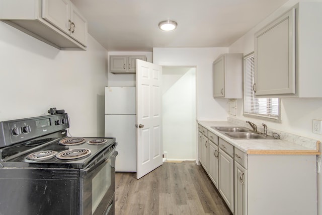 kitchen with light countertops, freestanding refrigerator, black electric range, light wood-style floors, and a sink