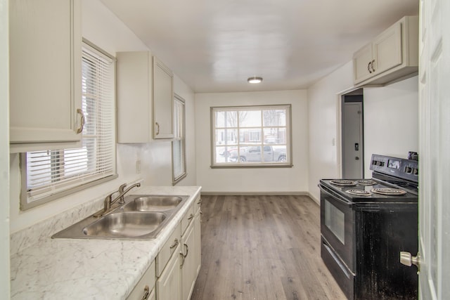 kitchen featuring baseboards, a sink, light countertops, light wood-style flooring, and black range with electric stovetop