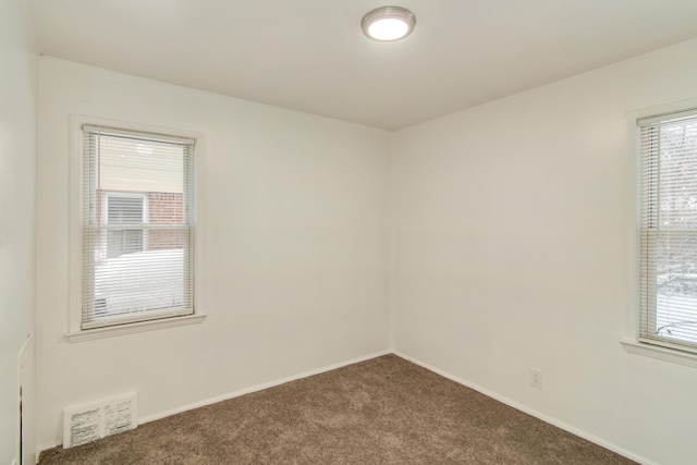 spare room with visible vents, baseboards, and dark carpet