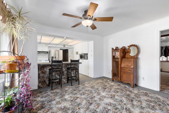 7190 Thornapple River Ct SE, Alto, MI 49302 - kitchen featuring dark colored carpet, ornamental molding, a ceiling fan, white cabinetry, and stainless steel appliances