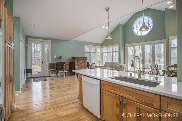 kitchen with a sink, light wood-style floors, white dishwasher, brown cabinetry, and hanging light fixtures