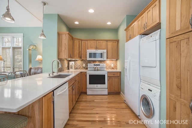 kitchen featuring a sink, white appliances, stacked washer / drying machine, light wood-style flooring, and a peninsula