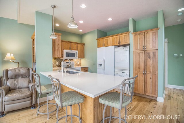 kitchen featuring a peninsula, stacked washer / dryer, backsplash, light wood-style floors, and white appliances