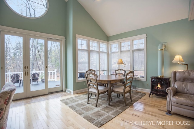 dining area with baseboards, high vaulted ceiling, a wood stove, and wood-type flooring