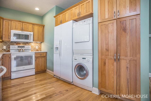 kitchen featuring light wood-type flooring, baseboards, decorative backsplash, white appliances, and stacked washer / drying machine