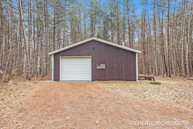 detached garage featuring driveway and a view of trees
