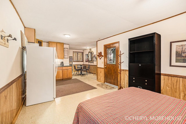 bedroom featuring crown molding, freestanding refrigerator, a wainscoted wall, and wood walls