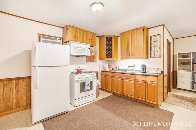 kitchen with brown cabinetry, dark countertops, a sink, and white appliances