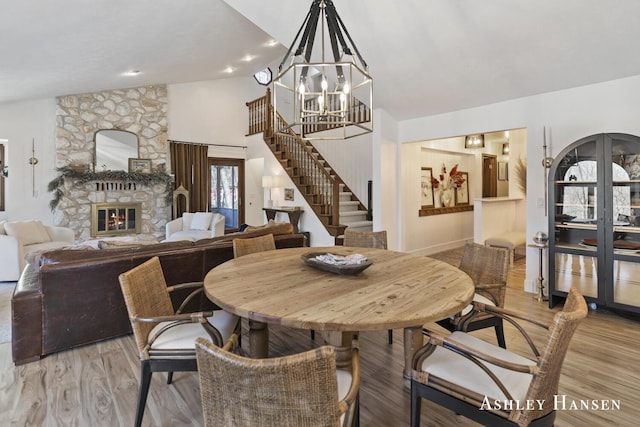 5615 Egypt Valley Ave NE, Belmont, MI 49306 - dining area featuring stairs, light wood-style flooring, a chandelier, a fireplace, and high vaulted ceiling