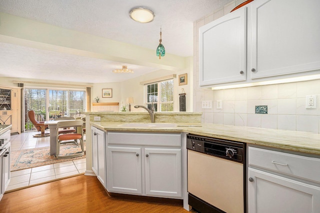 kitchen with white dishwasher, a sink, healthy amount of natural light, backsplash, and a textured ceiling