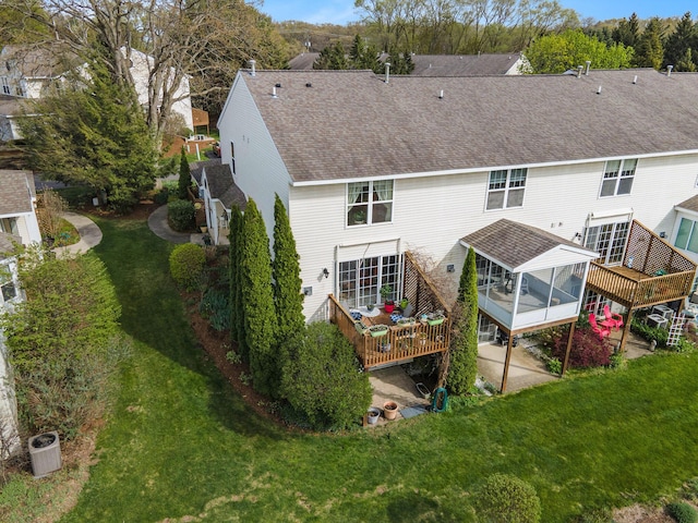 rear view of property with a deck, a sunroom, a shingled roof, and a yard