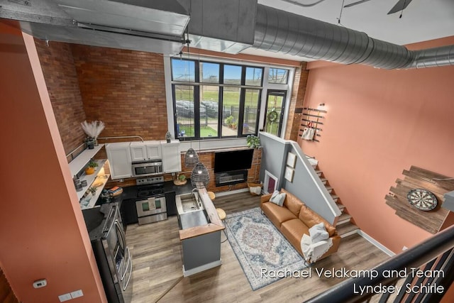 living area with a ceiling fan, baseboards, light wood-style flooring, stairs, and brick wall