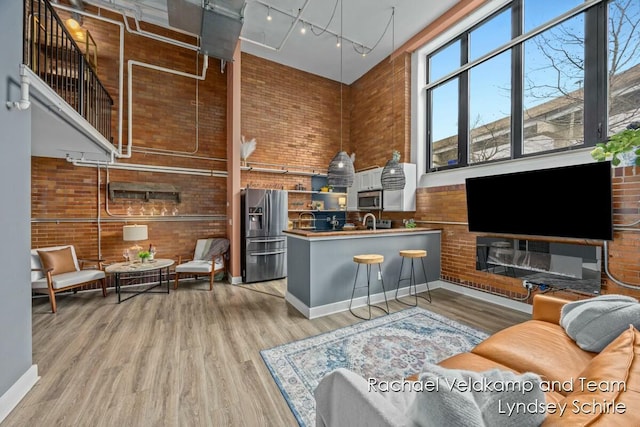 living room with track lighting, light wood finished floors, a towering ceiling, and brick wall