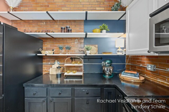 bar featuring stainless steel microwave, tasteful backsplash, and freestanding refrigerator