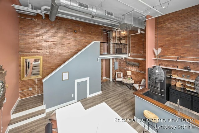 living area featuring wood finished floors, visible vents, baseboards, and brick wall