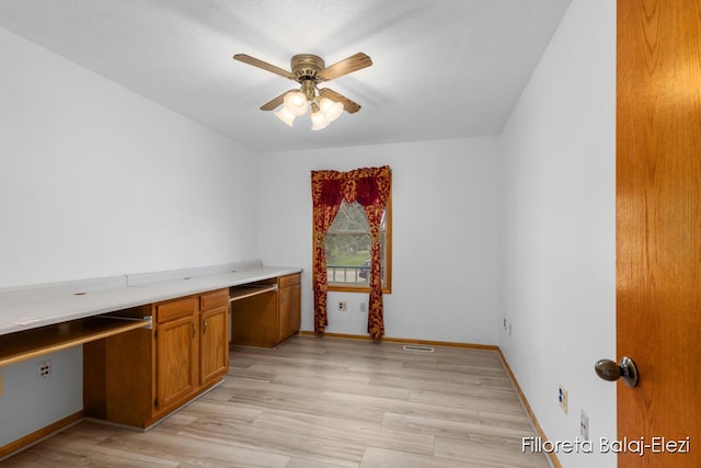 unfurnished office featuring ceiling fan, light wood-type flooring, visible vents, built in study area, and baseboards