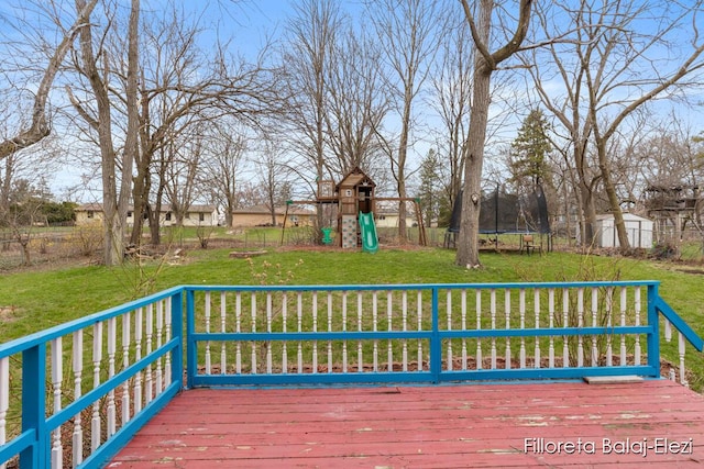 wooden terrace with a trampoline, a shed, an outbuilding, a playground, and a lawn