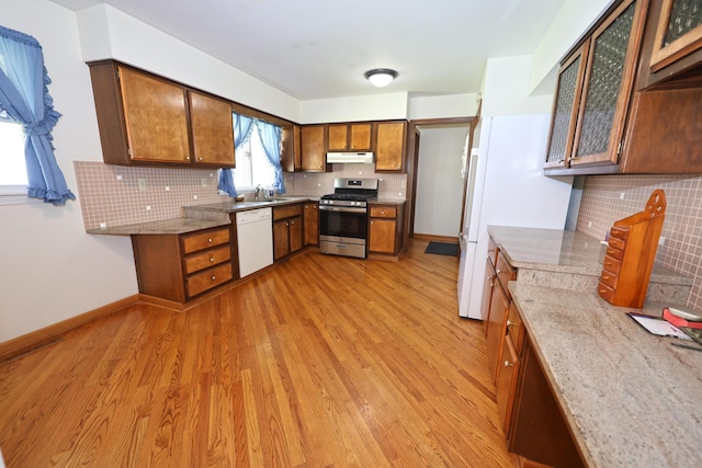 kitchen with under cabinet range hood, decorative backsplash, white dishwasher, stainless steel range with gas stovetop, and a sink