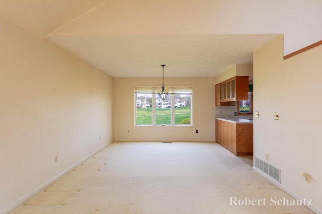 unfurnished dining area with an inviting chandelier, baseboards, light colored carpet, and visible vents