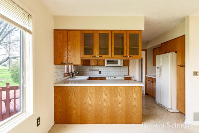 kitchen featuring a peninsula, brown cabinets, and white appliances