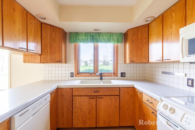 kitchen with brown cabinetry, white appliances, light countertops, tasteful backsplash, and a sink