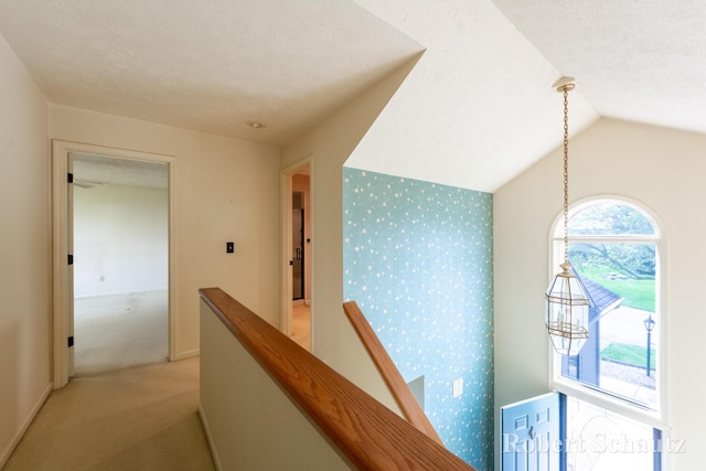 hallway featuring light colored carpet, wallpapered walls, an upstairs landing, and lofted ceiling