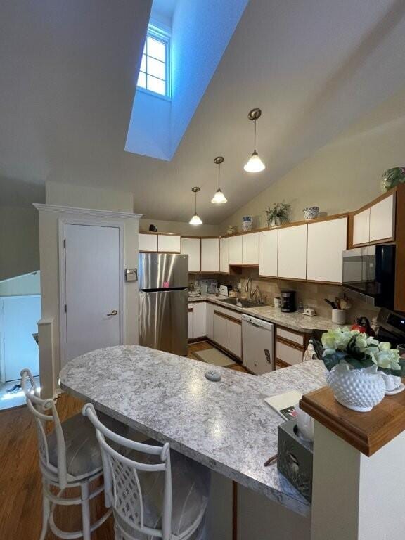 kitchen with a peninsula, white cabinets, a skylight, appliances with stainless steel finishes, and a sink