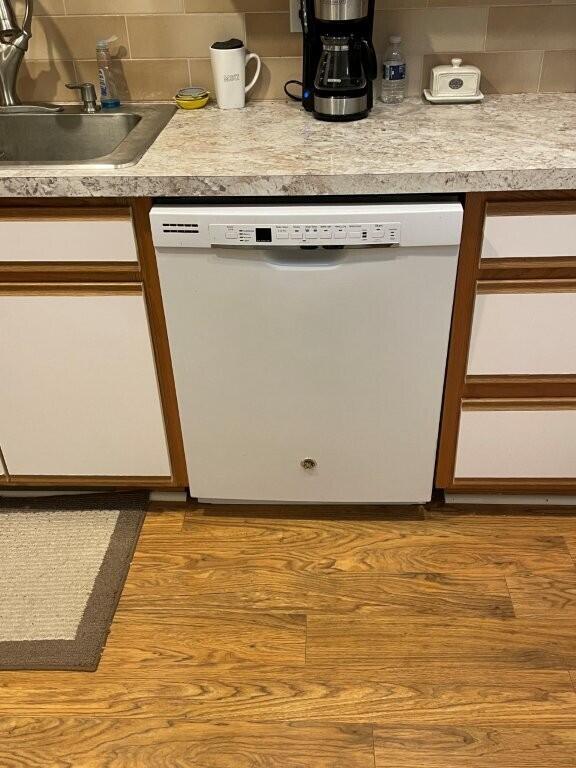 kitchen featuring white cabinetry, wood finished floors, dishwasher, a sink, and backsplash
