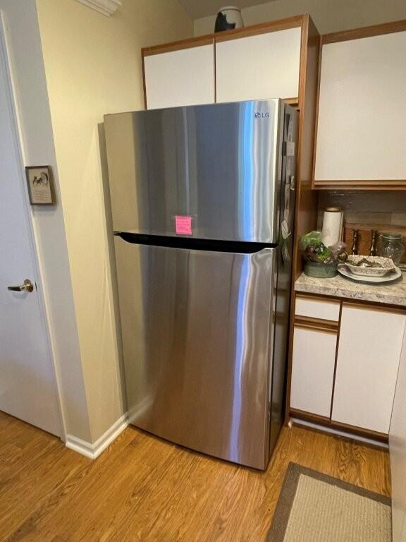 kitchen with light wood-style floors, freestanding refrigerator, and white cabinets