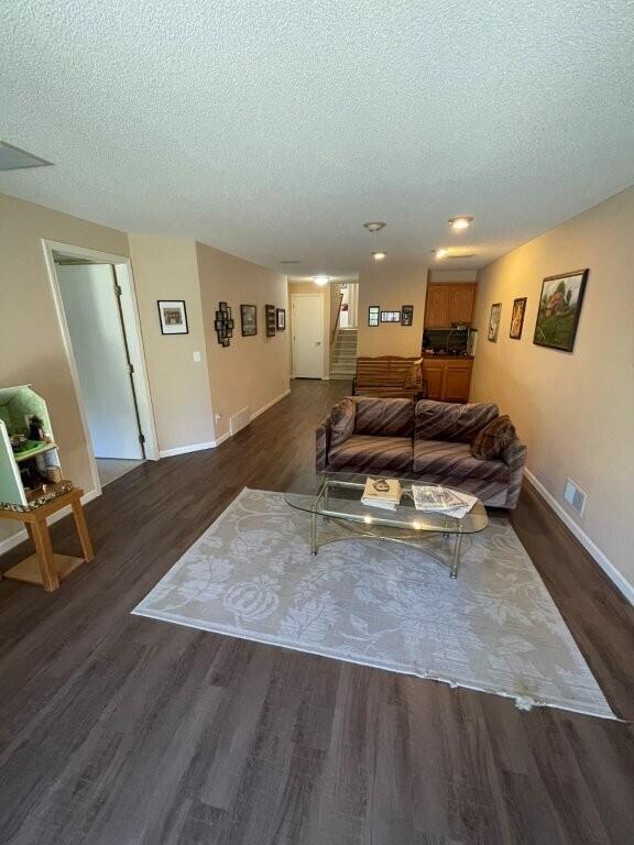 living area featuring visible vents, baseboards, wood finished floors, and a textured ceiling