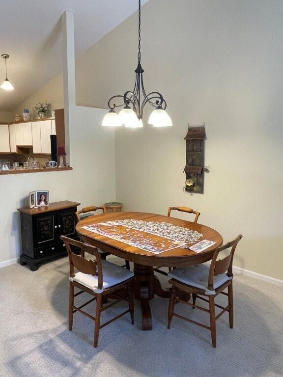dining area featuring a chandelier, baseboards, light carpet, and vaulted ceiling