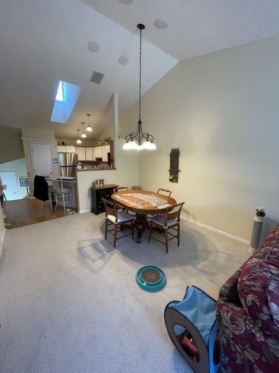 dining room featuring vaulted ceiling with skylight, visible vents, light colored carpet, and baseboards